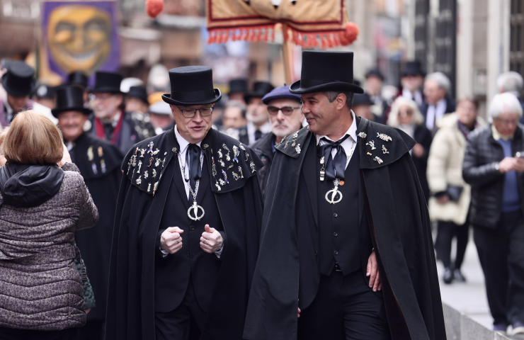 Dos hombres charlando vestidos de negro, con capa y sombrero en el desfile