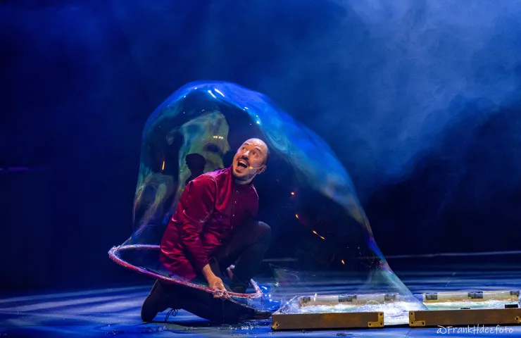 Un hombre en un escenario metido dentro de una gran pompa de jabón